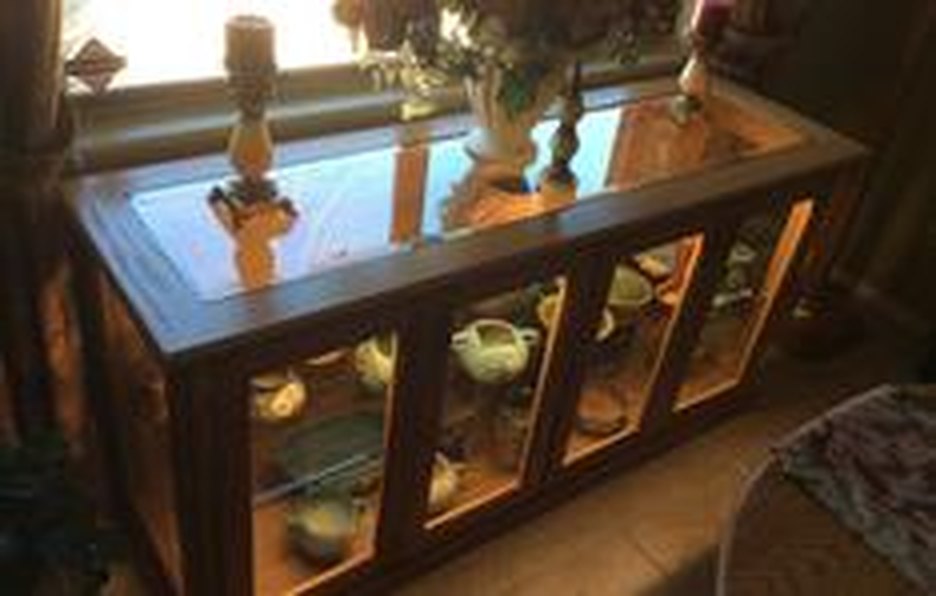 A lit display cabinet with glass doors and a glass top, holding glassware
