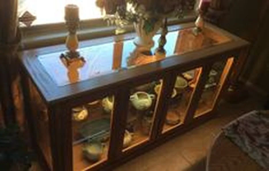 A lit display cabinet with glass doors and a glass top, holding glassware