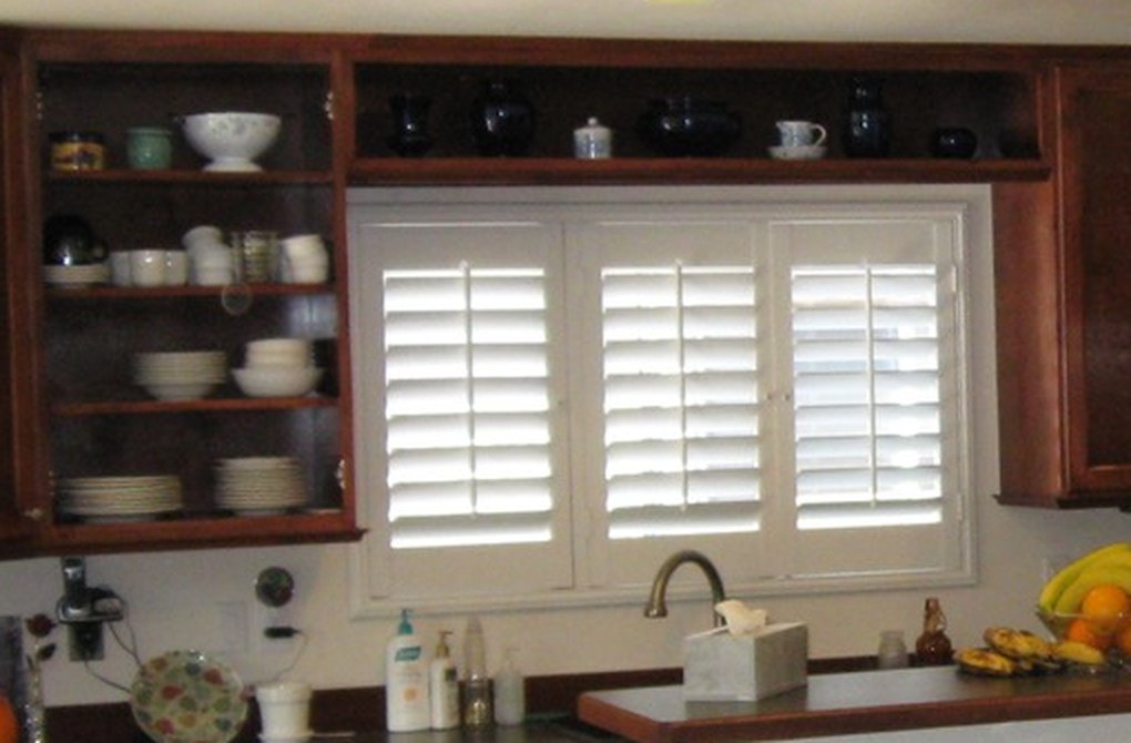 Open display shelving and a plate rack in stained cabinetry beside a shuttered window