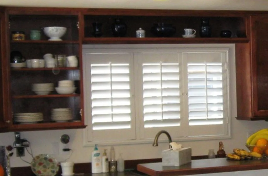 Open display shelving and a plate rack in stained cabinetry beside a shuttered window