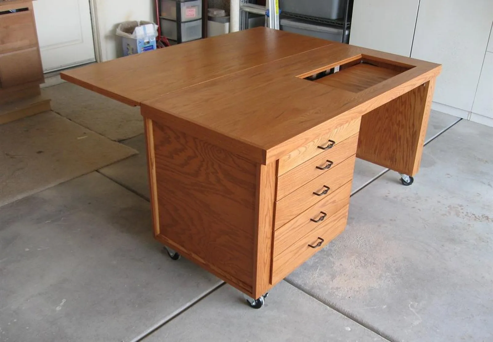 A custom oak work table with a fold out leaf, a bank of five drawers, and casters